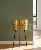Gold textured planter on black legs against a teal wall