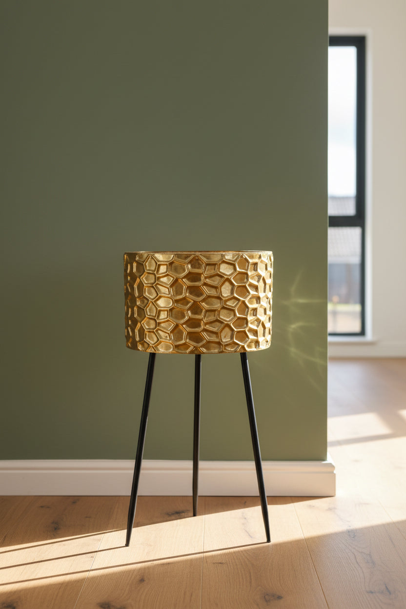 Gold textured planter on black legs against a teal wall