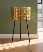 Gold textured table lamp on black legs against a green wall.