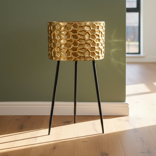 Gold textured table lamp on black legs against a green wall.