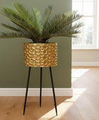 Gold textured plant pot with a plant and gold gorilla statue on a gray rug against a teal wall.