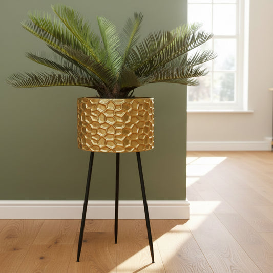 Gold textured plant pot with a plant and gold gorilla statue on a gray rug against a teal wall.