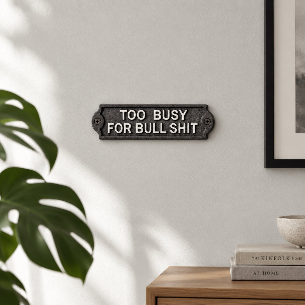 A rectangular cast iron sign with the text 'TOO BUSY FOR BULL SHIT' in raised white lettering, mounted on a dark gray surface.