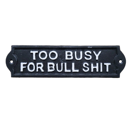 A rectangular black cast iron sign with raised white lettering that reads 'TOO BUSY FOR BULL SHIT', photographed against a rustic wooden surface.