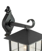 Black outdoor wall lantern with decorative arm on a white background