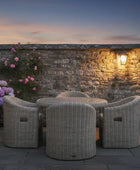 Outdoor patio set with wicker chairs and table against a stone wall at dusk.