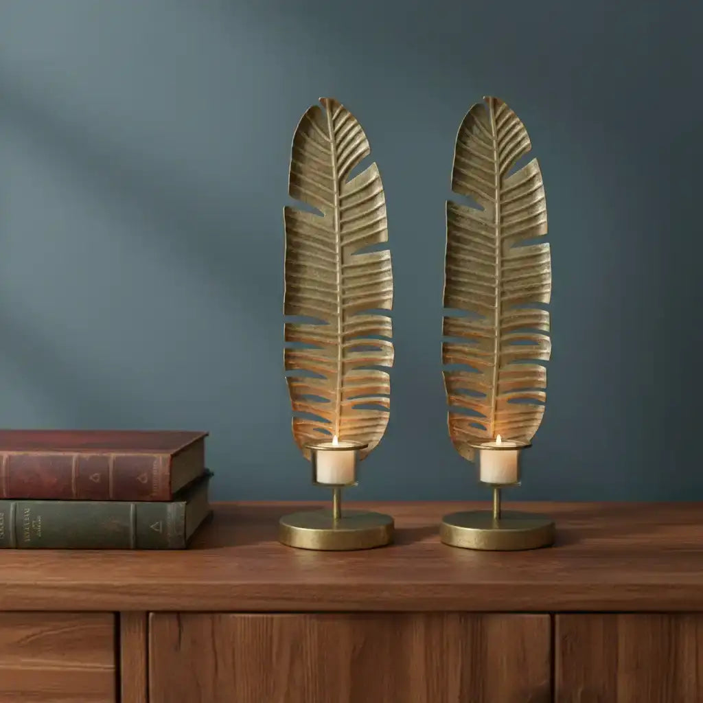 Two leaf-shaped candle holders on a wooden surface with a dark blue wall background