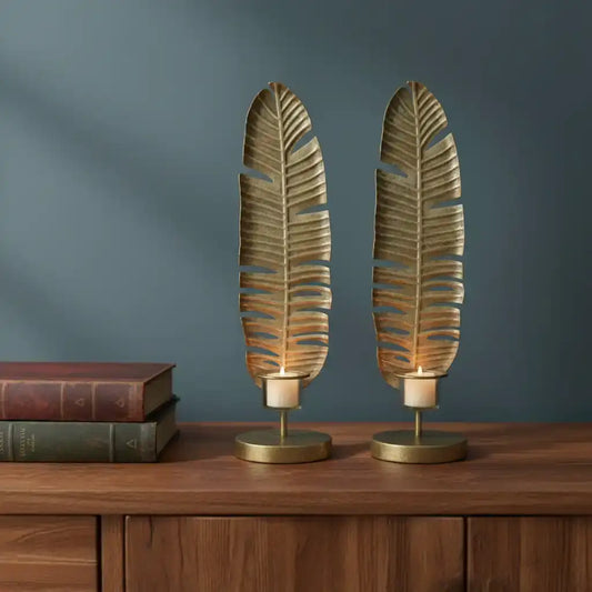 Two leaf-shaped candle holders on a wooden surface with a dark blue wall background