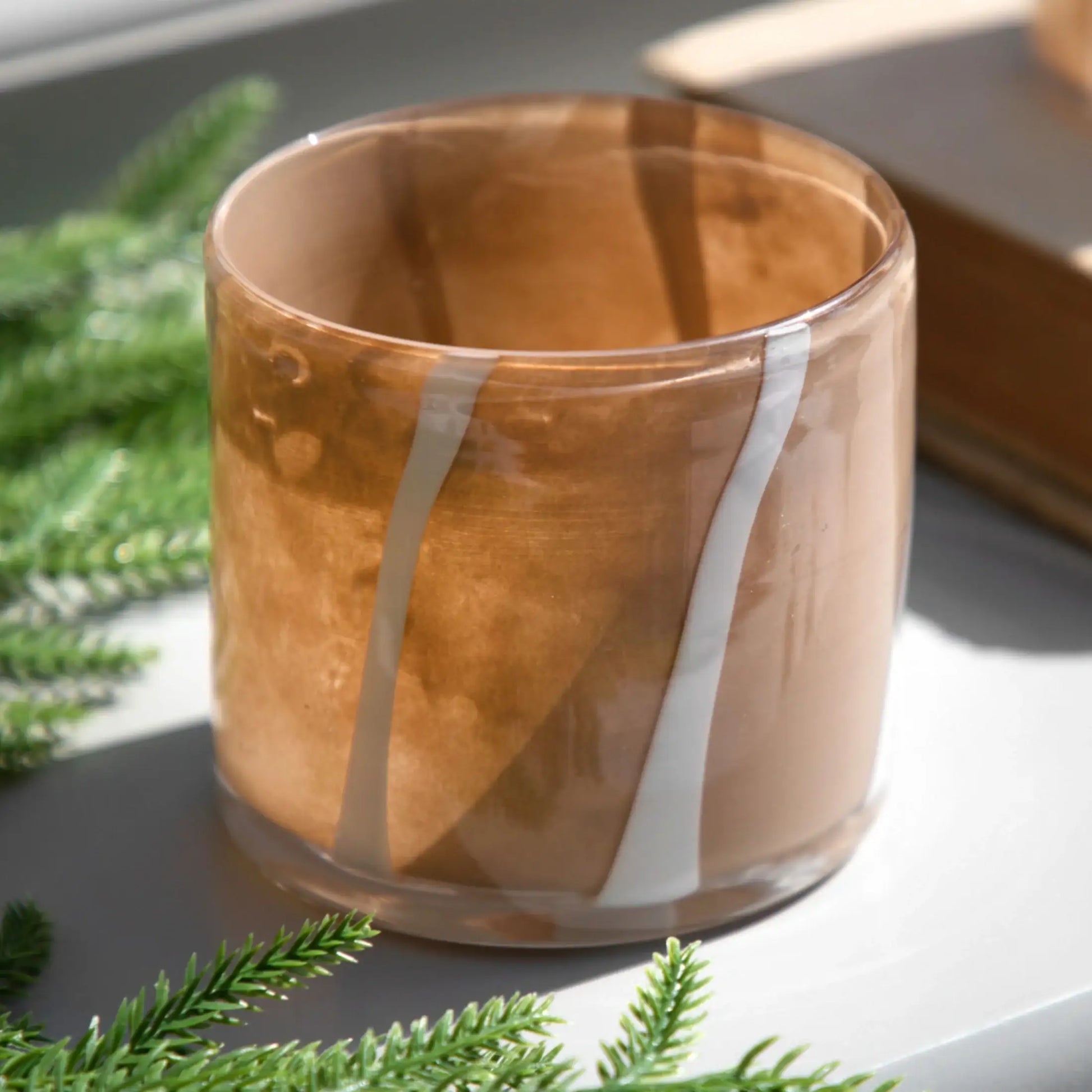 Glass candle holder with wooden finish on a surface with greenery