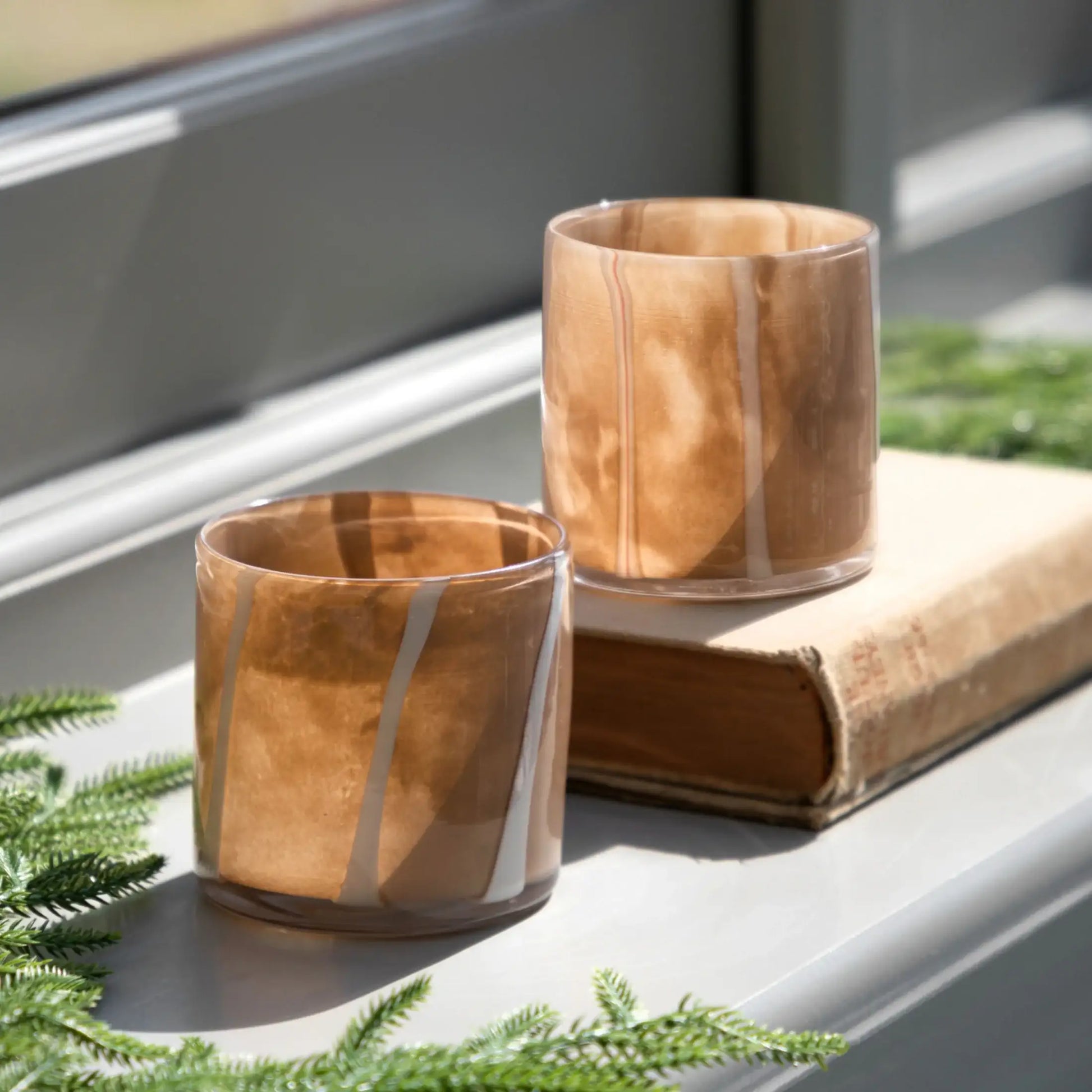 Two wooden-patterned glass tumblers on a windowsill with greenery.