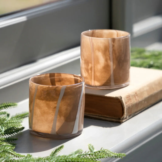 Two wooden-patterned glass tumblers on a windowsill with greenery.