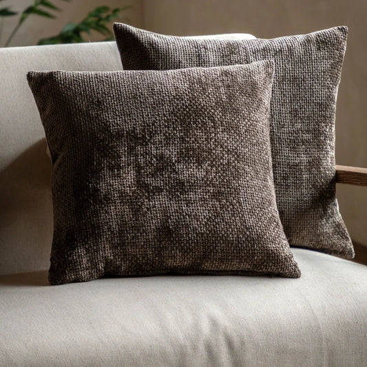 Two textured brown pillows on a light-colored sofa with a neutral background