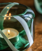 Candle in a green glass holder with white ribbons on a wooden surface