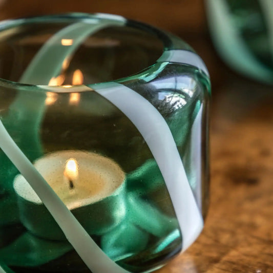Candle in a green glass holder with white ribbons on a wooden surface
