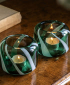 Two green glass candle holders with white ribbons on a wooden surface.