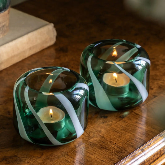 Two green glass candle holders with white ribbons on a wooden surface.