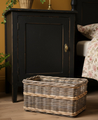 Black wooden cabinet with a wicker basket on a wooden floor next to a bed with floral bedding.