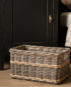 Wicker storage basket on a wooden floor next to a black cabinet.
