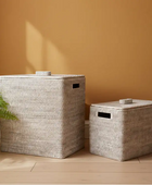 Two woven storage baskets with lids on a wooden floor against an orange wall.