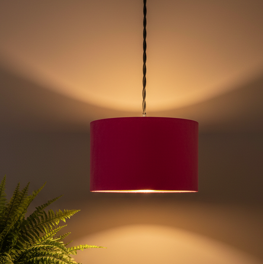 Red pendant light hanging against a neutral background with a plant on the left.