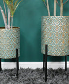 Two decorative planters with intricate patterns on a teal wall and gray carpet.