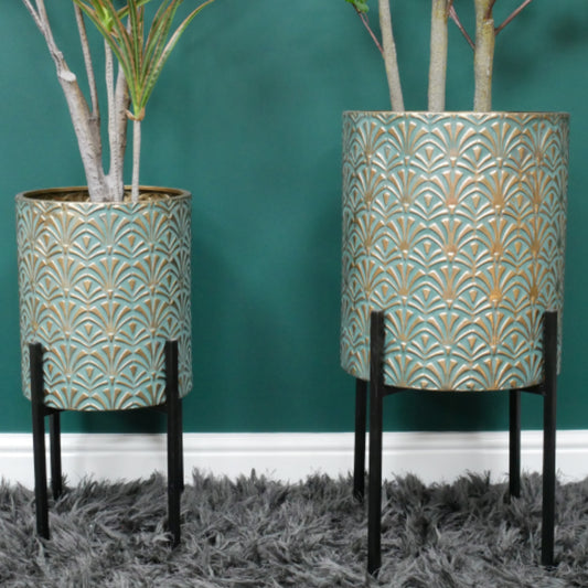 Two decorative planters with intricate patterns on a teal wall and gray carpet.
