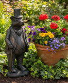 Statue of a bear in a suit next to a potted plant with flowers in a garden setting