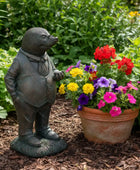 Statue of a mole in a suit next to a pot of colourful flowers in a garden setting
