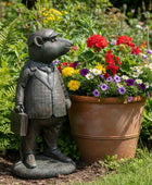 Statue of a mouse in a suit next to a potted plant with flowers in a garden setting