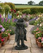 Statue of a frog in a suit in a garden with flowers and a table in the background