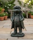 Garden statue of a frog in a suit on a stone patio with potted plants in the background