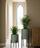 Two potted plants with decorative stands in a room with a window and framed picture.