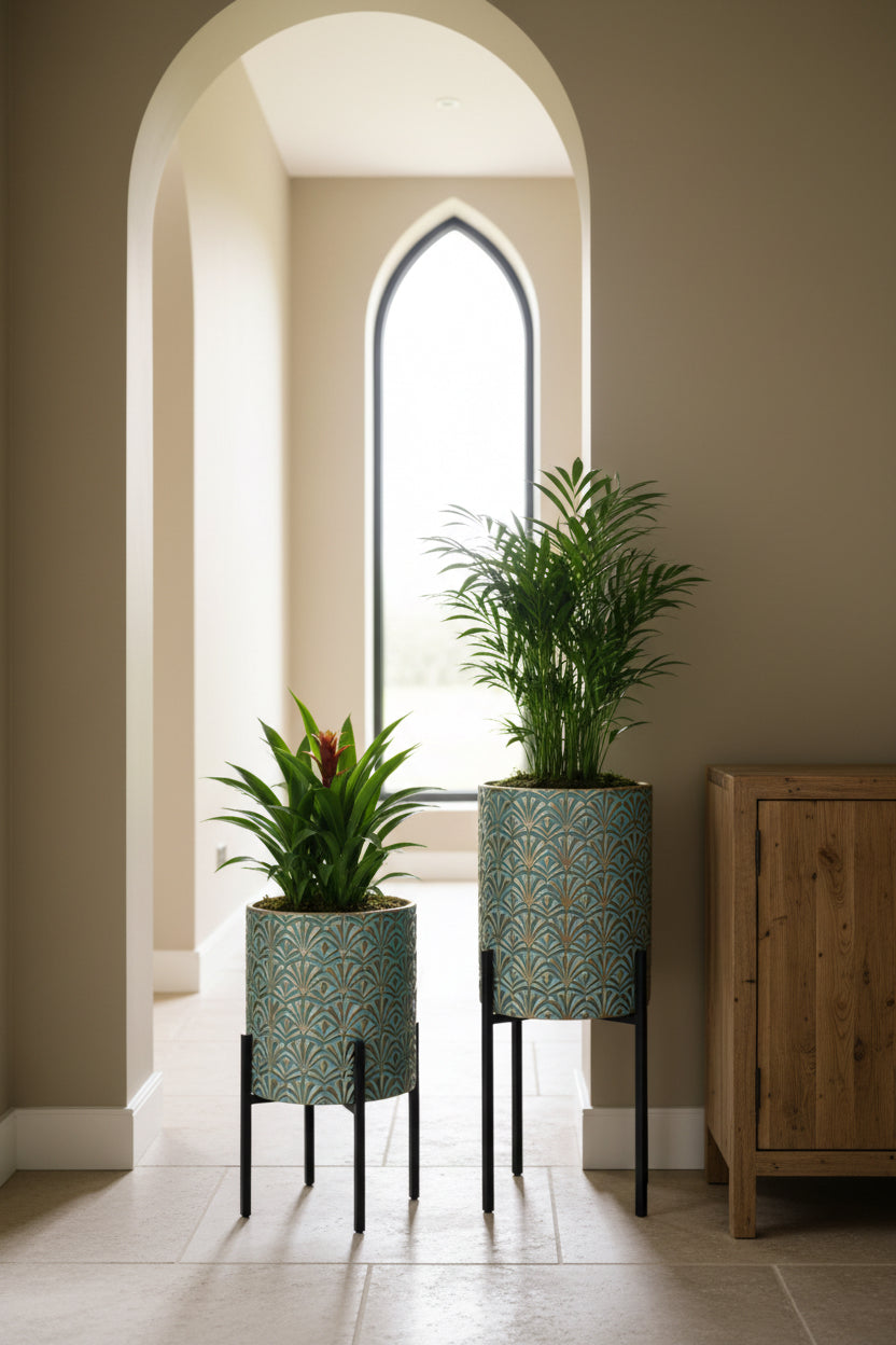 Two potted plants with decorative stands in a room with a window and framed picture.