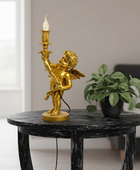 Gold angel lamp on a black marble table with a plant in the background