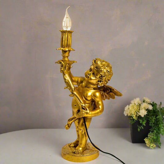Gold cherub lamp with a light bulb on a gray surface with a neutral background