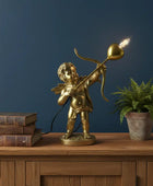 Gold cherub lamp with a light bulb on a wooden surface against a dark blue wall.