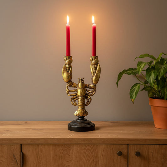 Gold lobster-shaped candle holder with two red candles against a stone wall.