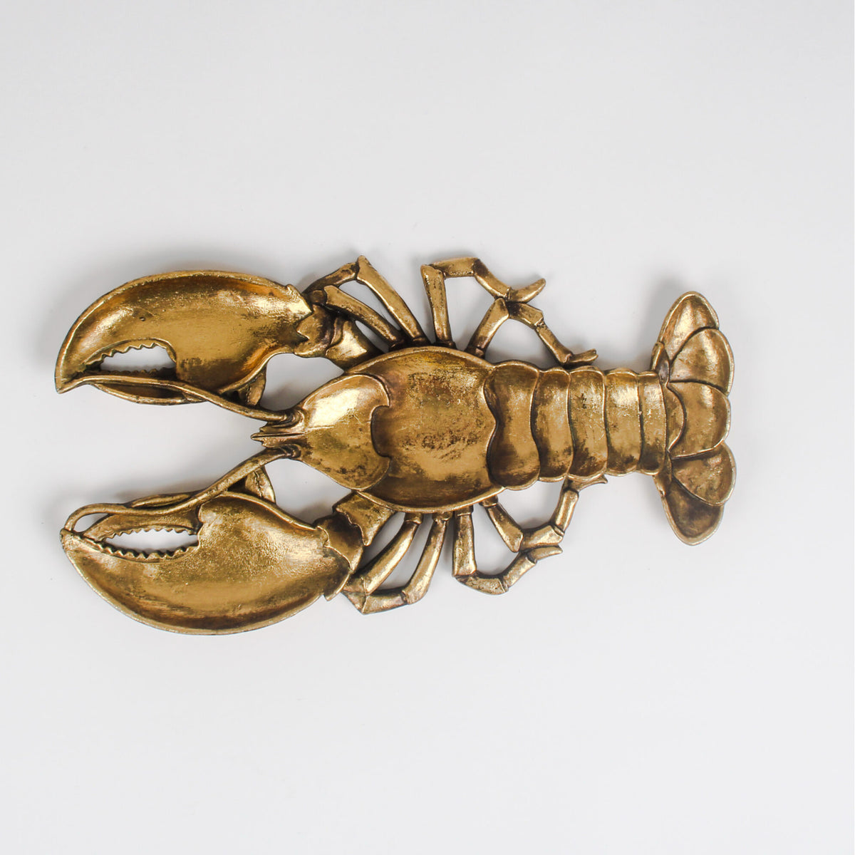 A metallic lobster-shaped decorative object with a warm gold/brass finish, photographed on a plain light gray background.