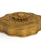An ornate antique-style gold box with a lid, featuring intricate floral engravings and a sunburst design on top, set against a plain white background.