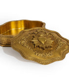 An ornate gold-toned metal box with a matching lid, featuring embossed floral scrollwork and a raised Sacred Heart design on the lid, photographed on a white background.