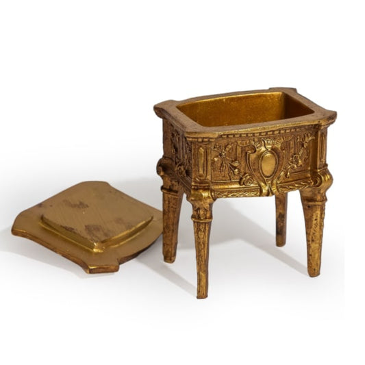 An ornate miniature gold-toned metal candelabra or decorative pedestal with a matching lid placed beside it, photographed on a clean white background.