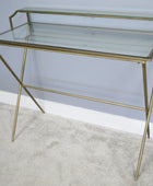 Glass console table with gold metal frame on a neutral background