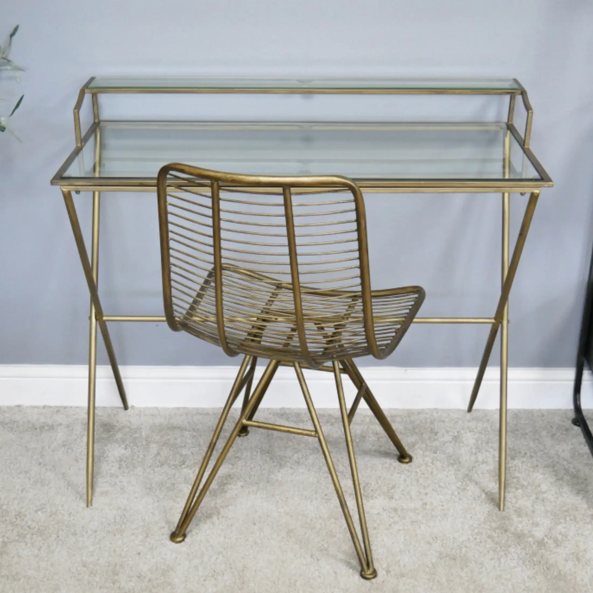 Gold metal desk with glass top and matching chair against a light gray wall.