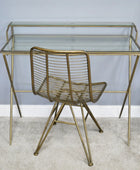 Gold metal desk with glass top and matching chair against a light gray wall.