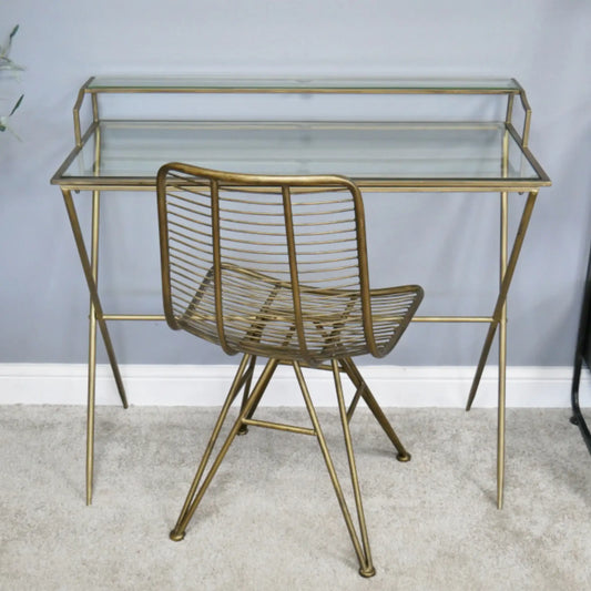 Gold metal desk with glass top and matching chair against a light gray wall.