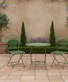 Green outdoor furniture set with table and chairs on a patio with decorative plants and wall.