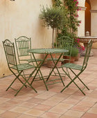 Green metal outdoor furniture set on a tiled patio with decorative plants and architecture.