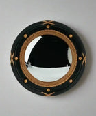 Round mirror with black frame and gold decorative elements on a plain wall.