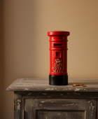 Red Royal Mail postbox on a wooden surface with a beige wall background
