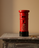 Red Royal Mail postbox on a wooden surface with a beige background